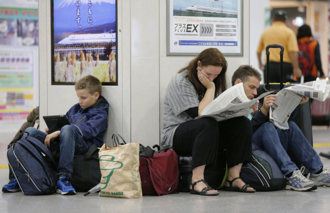 Tourists read newspapers while bullet train services are suspended because of a powerful typhoon at Tokyo Station on Monday.   AP-Yonhap
