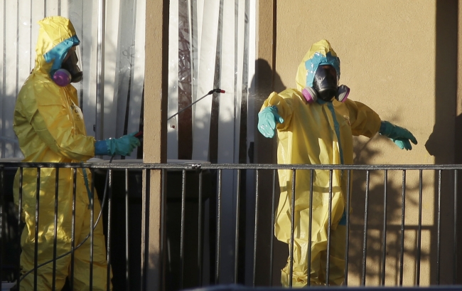 Hazardous material cleaners spray disinfectant on their personal protective equipment after working in the apartment where Thomas Eric Duncan, the Ebola patient who traveled from Liberia to Dallas, stayed last week.   AP-Yonhap