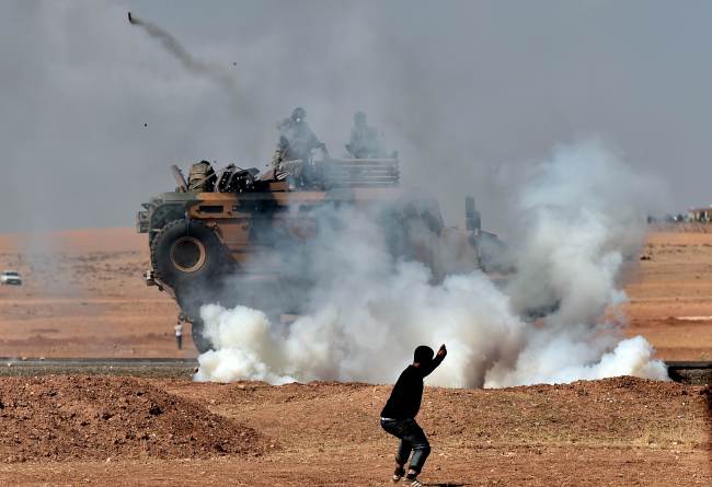 A Kurdish man throws stones at a Turkish armored vehicle firing tear gas as Turkish army soldiers try to remove people from the Turkish-Syrian border area near the Syrian town of Kobani in the southeastern town of Suruc, Sanliurfa province, Turkey, Tuesday.   AFP-Yonhap