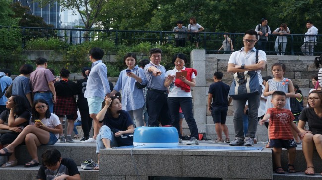 Passersby use a smartphone battery charging station at Cheonggyecheon Stream in downtown Seoul.   KEITI