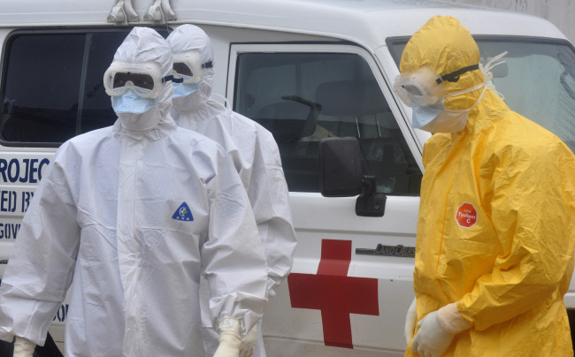 Health workers in protective gear wait to carry the body of a person suspected to have died from Ebola in Monrovia on Monday.   AP-Yonhap