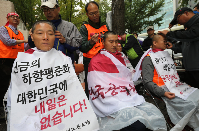 Unionized public servants shave their heads in protest against the government’s pension reform proposal in front of the government building in central Seoul on Monday.   Yonhap