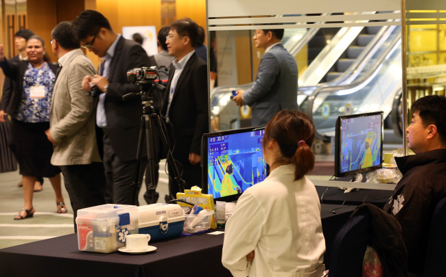 Officials at a forum organizing body monitor participants’ body temperatures at a hotel in Seoul on Monday. (Yonhap)