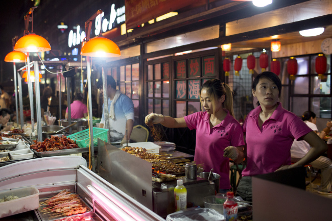 Women prepare food on the street in the Sanlitun area of Beijing.   Bloomberg