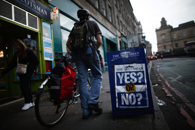 A pedestrian pushes a bicycle past a newsagent’s billboard with a poster for the Scotsman newspaper in Edinburgh, Scotland, Sept. 16.   Bloomberg