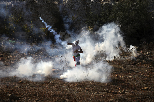 A Palestinian protester throws back a tear gas canister that was fired by Israeli troops during clashes at a protest in solidarity with demonstrators at the al-Aqsa mosque in Jerusalem, outside the Ofer military prison near the West Bank city of Ramallah, Tuesday.   AP-Yonhap