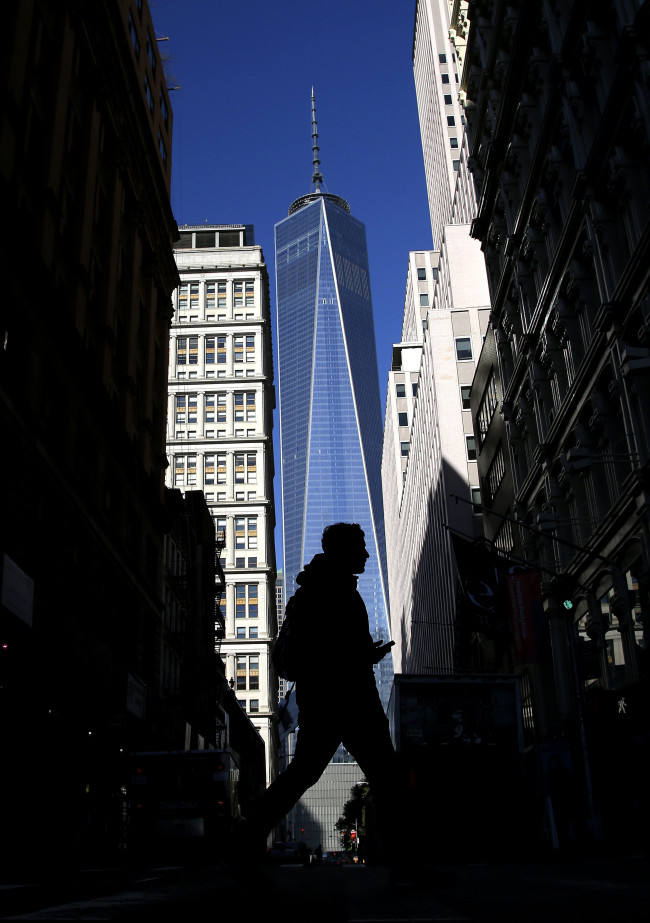 A man crosses the street in the shadows of One World Trade Center in New York City Monday.   UPI-Yonhap
