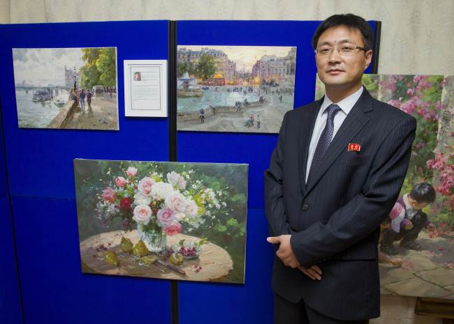 North Korean artist Jon Pyong-jin poses for a picture next to his paintings at the North Korean Embassy in London on Monday.   AFP-Yonhap