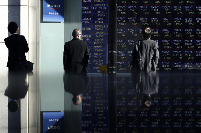 Pedestrians look at an electronic stock board outside a securities firm in Tokyo on Tuesday.   Bloomberg