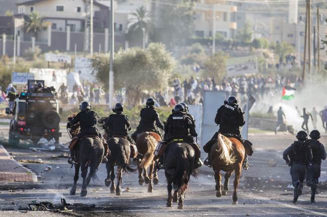 Israeli security forces ride their horses toward Arab-Israeli youths during clashes within the town of Kfar Kana in northern Israel on Sunday.   AFP-Yonhap