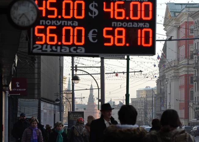 Pedestrians walk under a board listing foreign currency rates against the Russian ruble outside an exchange office in Moscow on Monday.   AFP-Yonhap