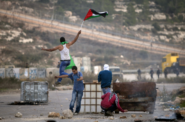 A Palestinian demonstrator holding a national flag jumps during clashes with Israeli soldiers outside the Ofer military prison near the West Bank city of Ramallah on Tuesday.   AP-Yonhap