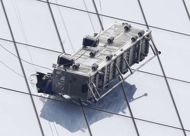 A firefighter reaches through a cut-out window into a dangling work basket to rescue two workers from the 60th floor of 1 World Trade Center in New York on Wednesday.   AP-Yonhap
