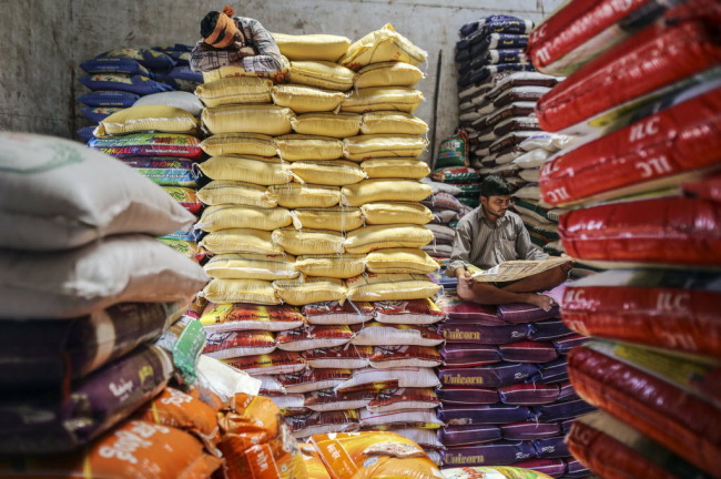 Workers sit and lie on stacked bags of rice at a wholesale market in Mumbai, India.   Bloomberg