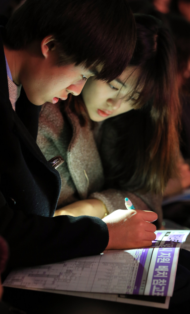 Students look at a table of cutoff scores for university applications at a college entrance information session at Jamsil Indoor Stadium in Seoul on Monday.   Yonhap