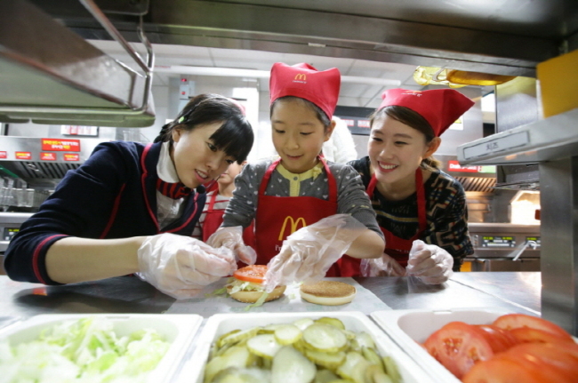 Kim Young-a, a McDonald’s Korea restaurant manager, helps a young customer make a burger at an outlet in Gwanhun-dong, Seoul, on Friday.   McDonald’s Korea