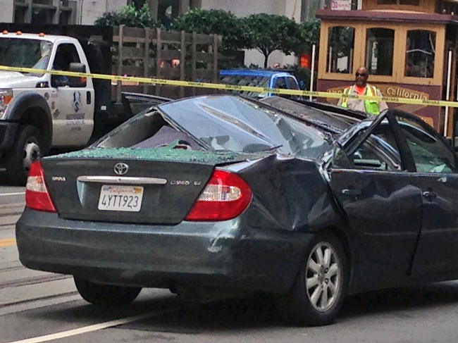 Police and citizens look over a car that has a caved in roof after a window washer fell at least 11 stories onto a moving vehicle in San Francisco on Friday.   AP-Yonhap