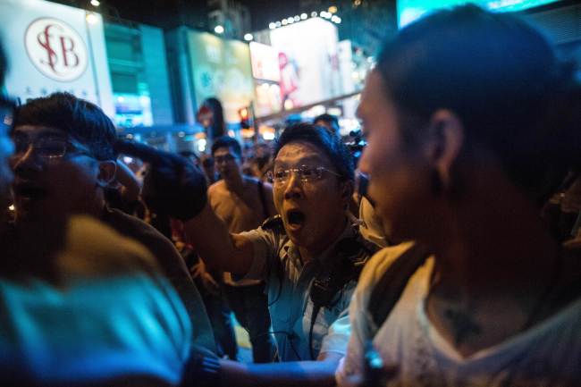 A police officer (center) pushes pro-democracy protesters out of a road during an attempt by members of the movement to occupy a major protest site that was cleared by police in the Mong Kok district of Hong Kong on Wednesday.   AFP-Yonhap