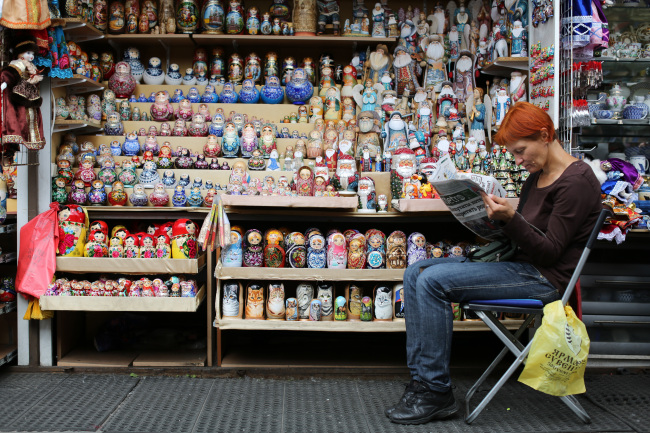 A vendor reads a newspaper beside a souvenir stand selling matryoshka dolls in St. Petersburg, Russia.  Bloomberg