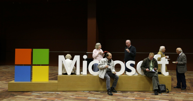 Attendees of Microsoft Corp.’s annual shareholders meeting sit on a Microsoft sign in Bellevue, Washington, last week.   AP-Yonhap
