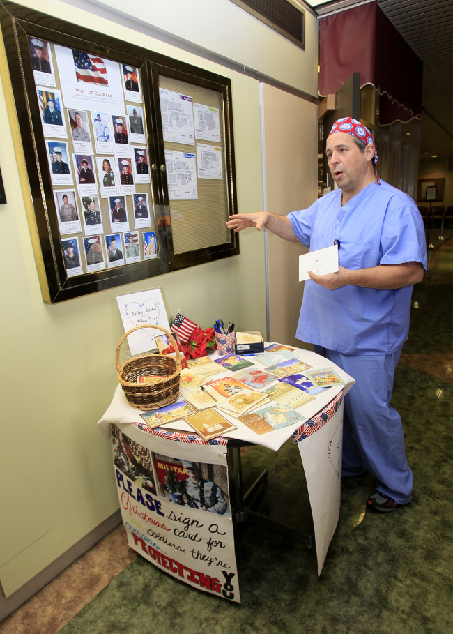 Tom Stiles, a surgical assistant at Summa Barberton Hospital, talks about his effort to send holiday cards to those in military service overseas as he stands next to a table he set up for people to write cards to members of the military at the entrance of the hospital in Barberton, Ohio on Nov. 19. (Akron Beacon Journal/TNS)