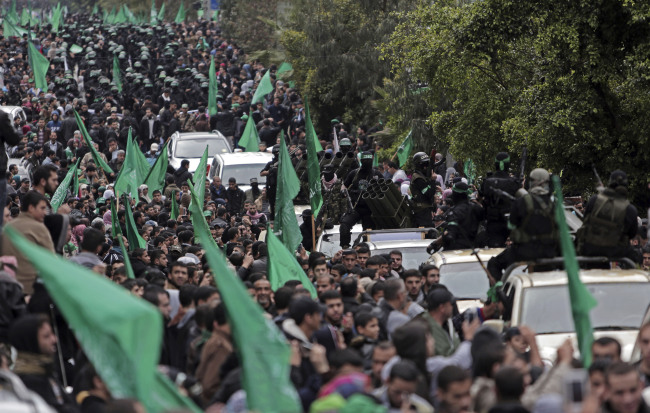Palestinians gather around Hamas masked members displaying their military skills during a rally to commemorate the 27th anniversary of the Hamas militant group in Gaza City on Sunday.   AP-Yonhap