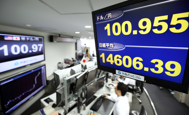 Employees work beneath a monitor displaying the yen-dollar exchange rate in Tokyo.    Bloomberg