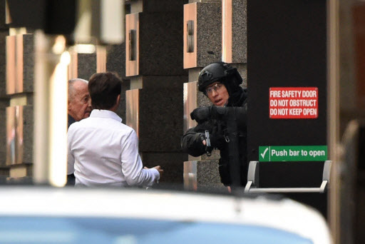 Two hostages (L) run for cover behind a policeman (R) during a hostage siege in the central business district of Sydney. (AFP)