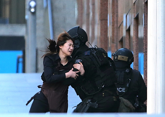A hostage runs to armed tactical response police officers for safety after she escaped from a cafe under siege at Martin Place in the central business district of Sydney, Australia, Monday.    AP-Yonhap