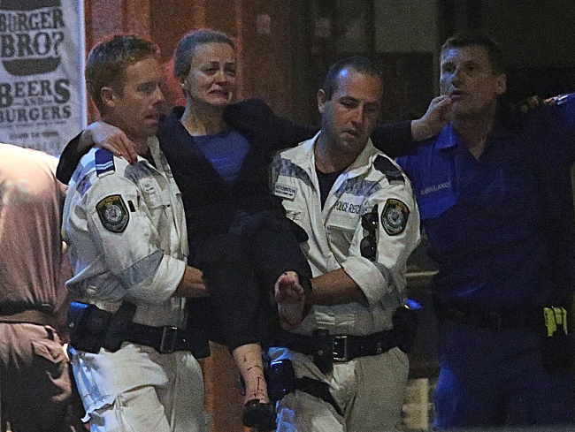 An injured hostage is carried to an ambulance after shots were fired during a cafe siege at Martin Place in the central business district of Sydney, Australia, Tuesday.   AP-Yonhap