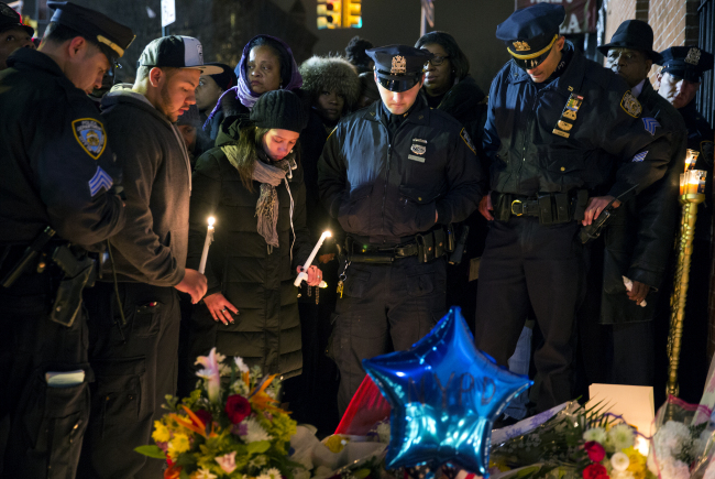 Police officers and other mourners stand in silence, Sunday, during a candlelight vigil near the spot where two New York Police Department officers, sitting inside a patrol car the previous day, were shot by an armed man, killing them both.    AP-Yonhap