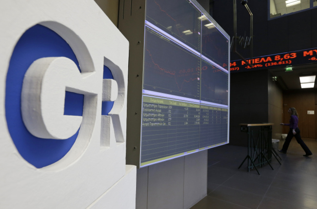 An employee of the Stock Exchange walks by a display board showing losses for Greek shares in Athens on Monday.   AP-Yonhap