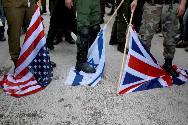 Members of the al-Aqsa Martyrs Brigades, the Palestinian Fatah movement’s armed wing, step on U.S., Israeli and British national flags during a rally marking the 50th anniversary of the movement’s creation in the Aida refugee camp, near the West Bank city of Bethlehem, Friday.    AFP-Yonhap