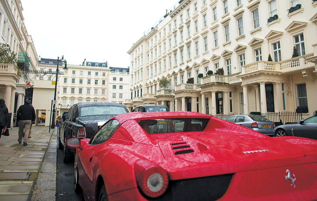 Pedestrians pass a red Ferrari luxury automobile parked on Eaton Place in the Kensington district of London. (Bloomberg)