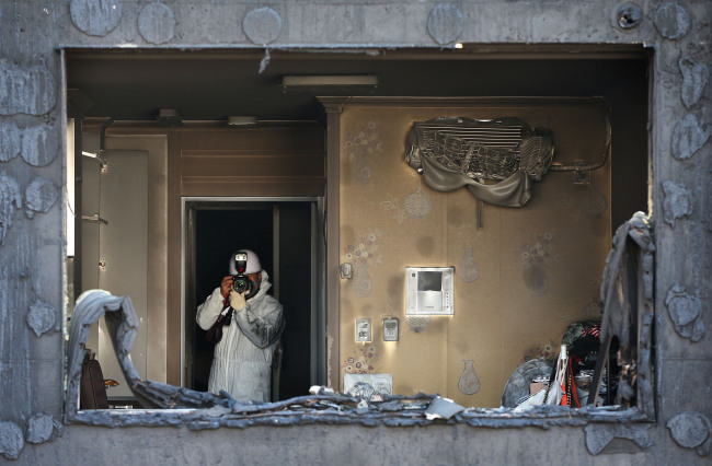 An investigator takes photos of a scorched apartment building in Uijeongbu, Gyeonggi Province, Monday, as part of efforts to determine the cause of the fire on Saturday that left four residents dead and 126 others wounded.   Yonhap