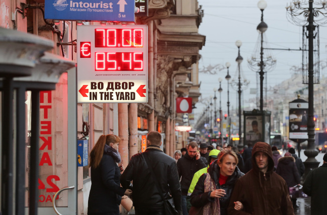 Pedestrians pass a currency exchange rate sign on Nevsky Prospekt shopping street in St. Petersburg, Russia.   Bloomberg