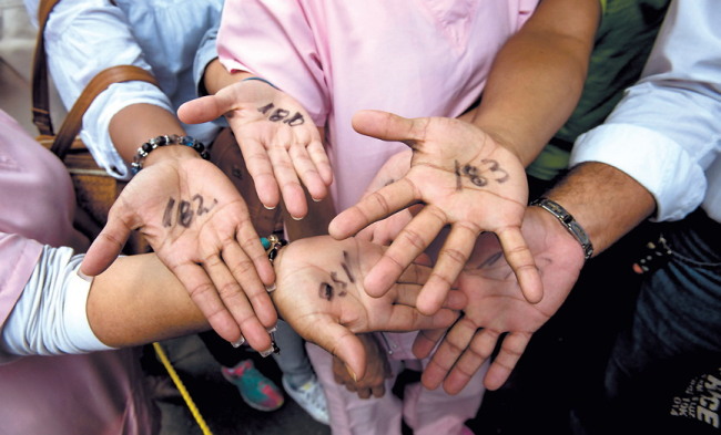 People show their respective waiting line assigned numbers written on their palms as they queue up outside a supermarket to buy food, in Caracas. (Yonhap)