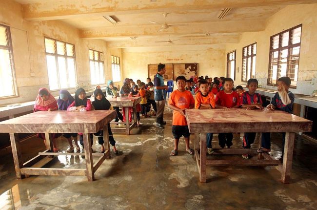 Pupils of SK Manek Urai starting their first day in school with whatever furniture was left by the floods.   The Star
