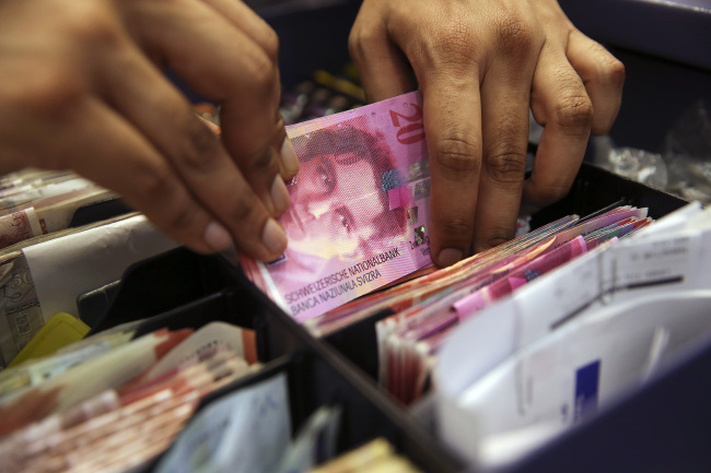 An employee places a bundle of Swiss franc banknotes into a cashier’s tray at a store in London.   Bloomberg