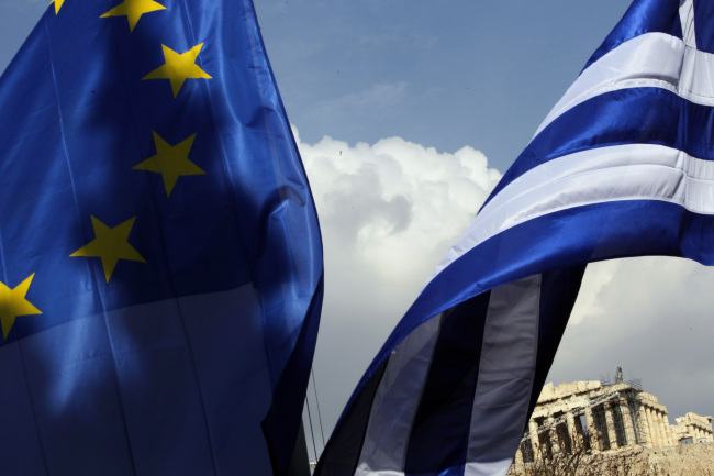 A European Union flag and a Greek national flag fly beneath the Parthenon temple on Acropolis hill in Athens, Greece.    Bloomberg