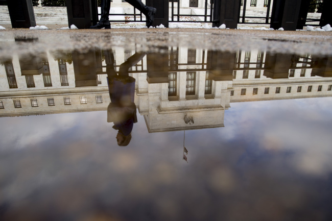A woman walks past the Federal Reserve building as it is reflected in a puddle of water in Washington, D.C.   Bloomberg