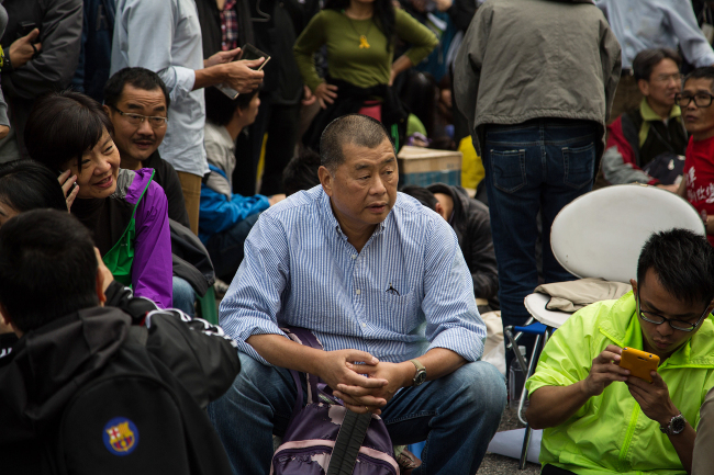 Jimmy Lai, chairman of Next Media Ltd. (center) sits among protesters outside the Central Government Offices in the Admiralty district of Hong Kong on Dec. 11.   Bloomberg