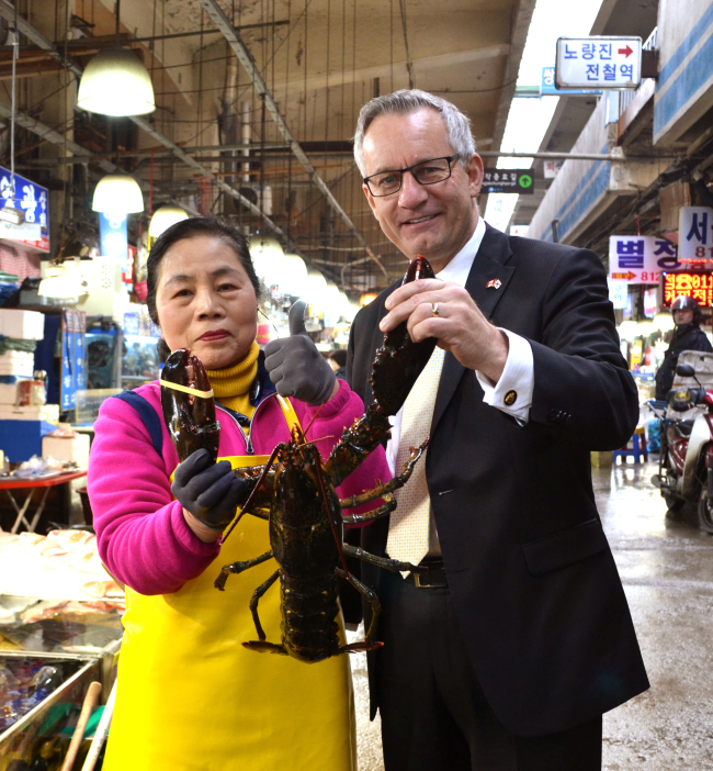 Ed Fast (right), Canada’s international trade minister, poses with a vendor and a Canadian lobster at the Noryangjin Fisheries Wholesale Market in Seoul last week.   Ed Fast Flickr