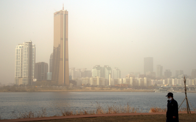A man with a protective mask walks along the Hangang River, where visibility remained low due to high levels of yellow dust in central Seoul on Monday.     Yonhap