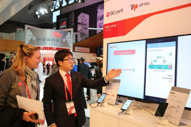 BC카드 관계자(오른쪽)가 스페인 바르셀로나에서 열리고 있는 MWC 2015를 참관하는 외국인에게 실물카드를 스마트폰에 터치하여 결제하는 탭사인(TapSign) 서비스를 설명하고 있는 모습 [사진=BC카드]