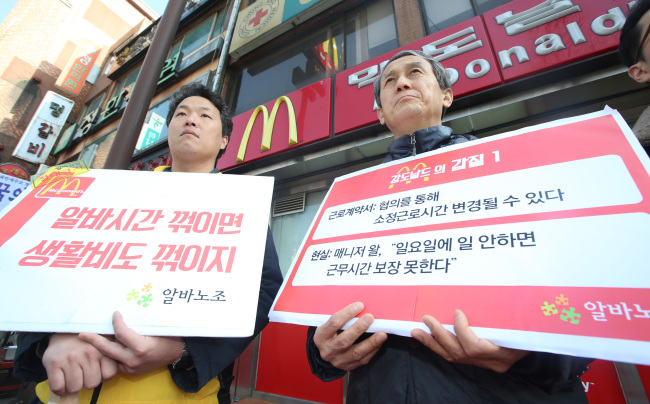 Two members of the union of part-time workers hold up signs protesting against McDonald’s alleged arbitrary roster adjustments in Seoul last week. Yonhap