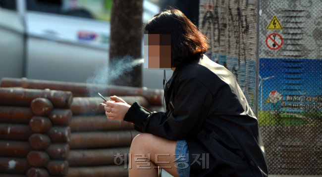 한 10대 여학생이 길가에 앉아 담배를 피우며 스마트폰을 보고 있다. 김명섭 기자/msiron@heraldcorp.com