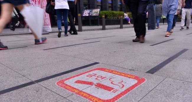 Pedestrians pass a “no smoking” sign in Gangnam, southern Seoul.   Lee Sang-sub/The Korea Herald