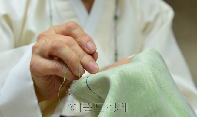 그의 반짓고리에는 고운 색색의 실이 둥그렇게 감겨 바늘에 꿰어지길 기다리고 있다. 그는 그 중 녹색 실을 골라 바늘에 꿰었다. 작은 바늘 구멍을 찾느라 눈을 조리개 맞추듯 할 필요없이 바늘 꿰어주는 도구를 사용했다. 그리고 왼손에 짓다 만 고운 색동저고리를 들고 솔기를 붙여나가기 시작했다. 눈을 감고도 할 수 있는 침선의 세월이지만 그는 묵묵히 조심스럽게 바느질을 이어갔다. 사진=윤병찬기자/yoon4698@heraldcorp.com