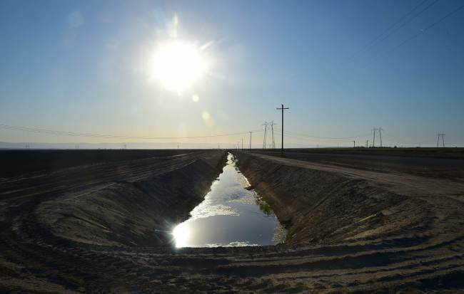 Water flows along a canal near fields of crops beneath the sweltering sun in Kern County, California.   AFP-Yonhap